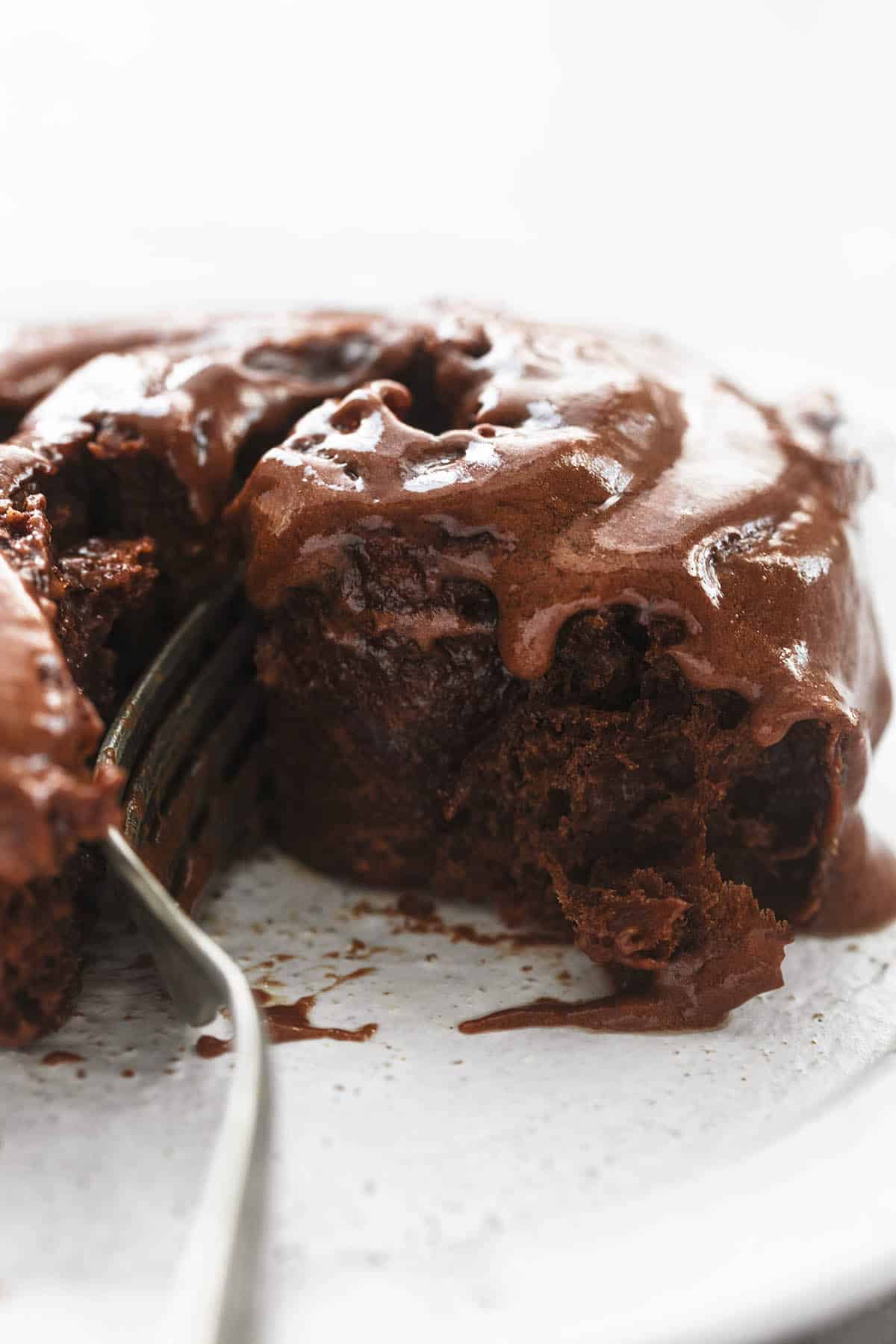 close up of a chocolate cinnamon roll with hazelnut icing and a fork.