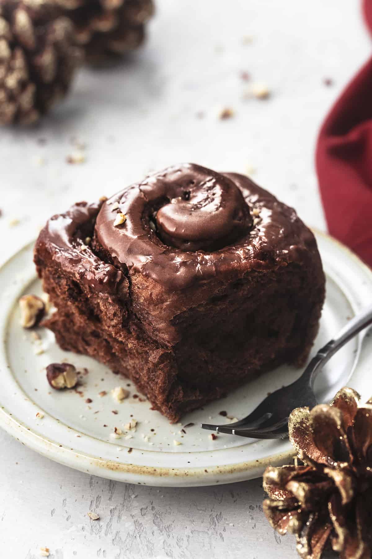 close up of a chocolate cinnamon roll with hazelnut icing with a fork on a plate.