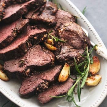 up close view of sliced beef tenderloin on serving platter with whole garlic cloves and rosemary