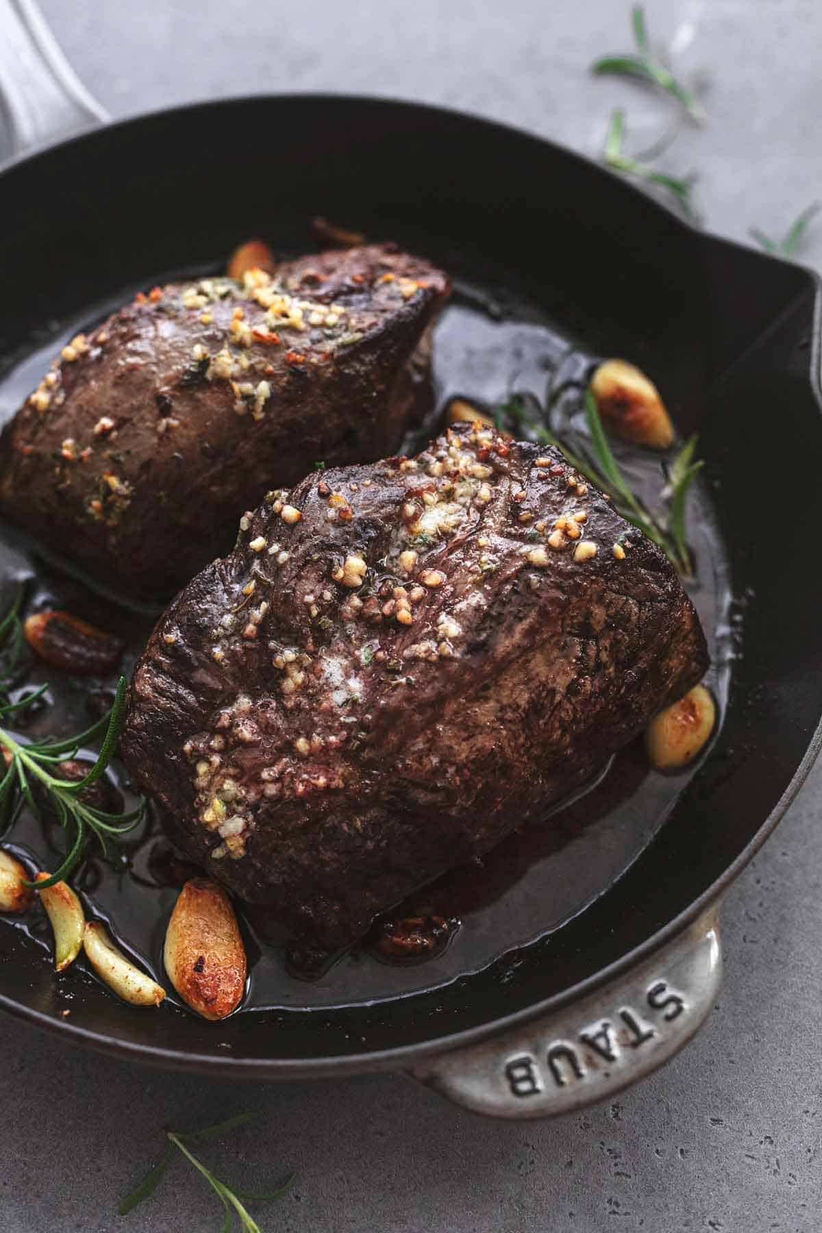 roasted garlic butter beef tenderloin with garlic cloves and rosemary in skillet.