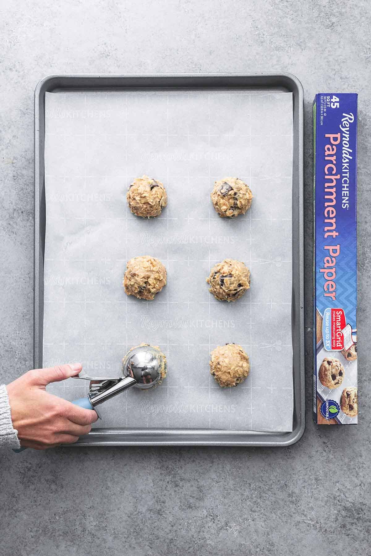 top view of a hand dropping scoops of chunky monkey banana cookie dough onto a parchment-lined baking sheet.
