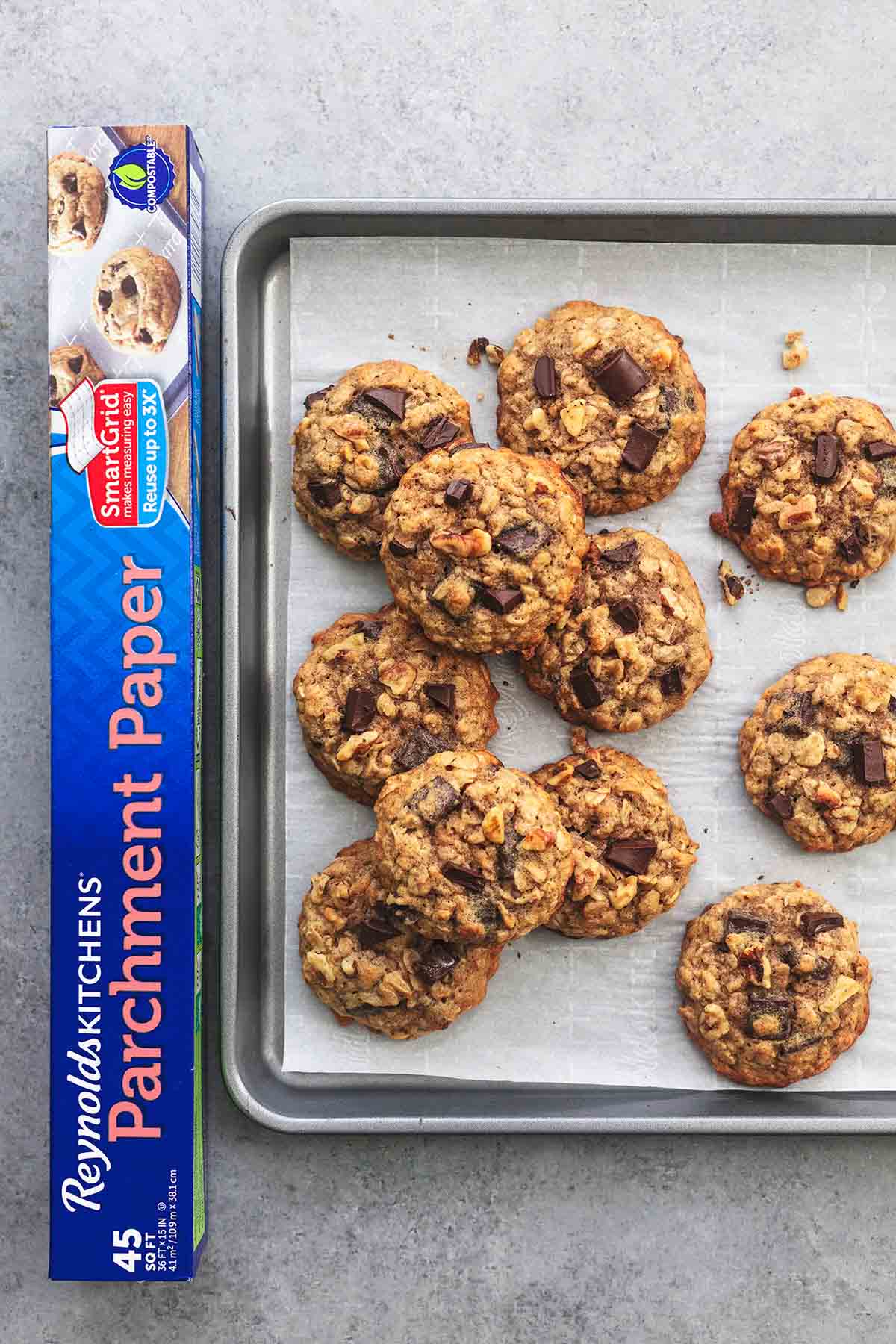 top view of chunky monkey banana cookies on a baking sheet beside a box of parchment paper.