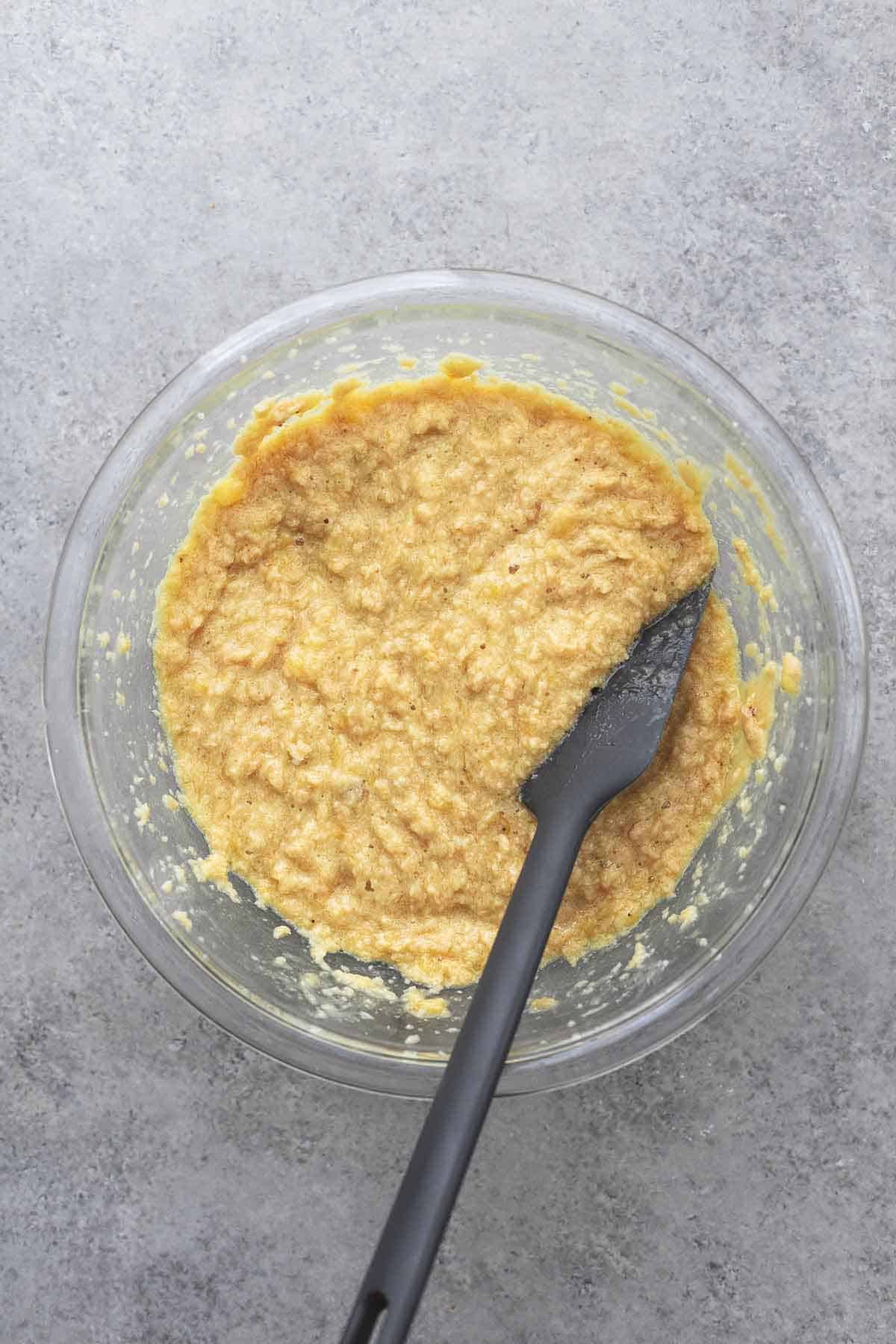 top view of mixed yellow cookie batter in a glass bowl with a gray spatula.