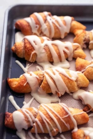baked cinnamon sugar crescent roll ups with icing on sheet pan