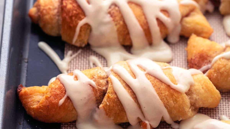 baked cinnamon sugar crescent roll ups with icing on sheet pan