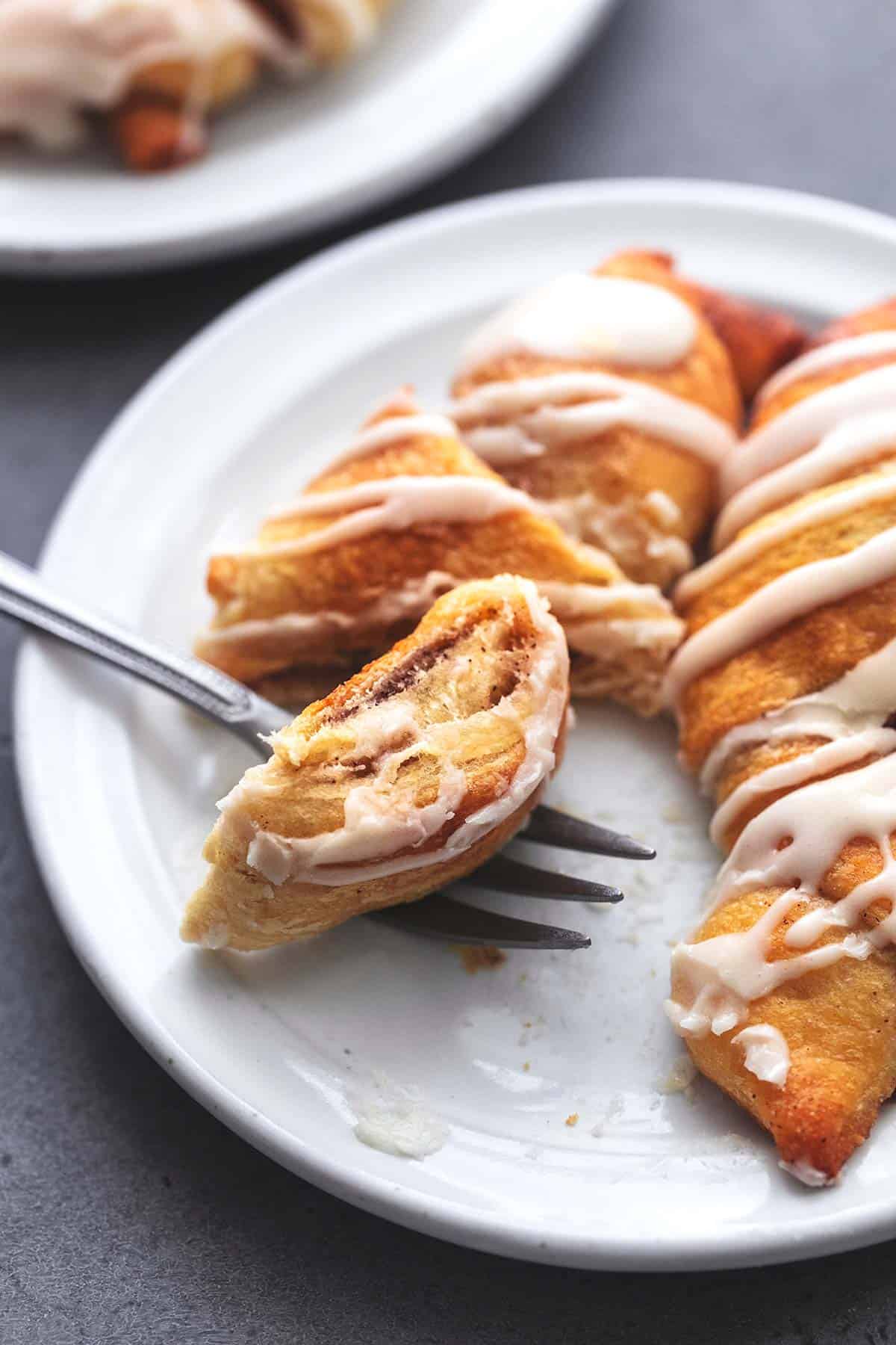 close up of a bite of a cinnamon roll up on a fork with more roll ups on the side all on a plate.