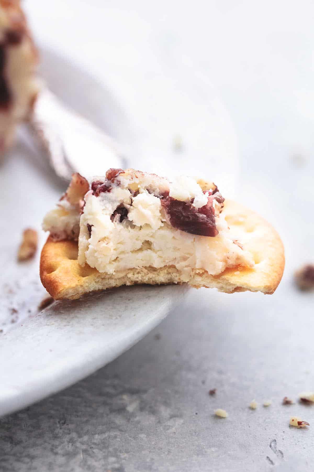 close up of a cracker with cranberry pecan cheeseball on top with a bite missing resting on the edge of a plate.
