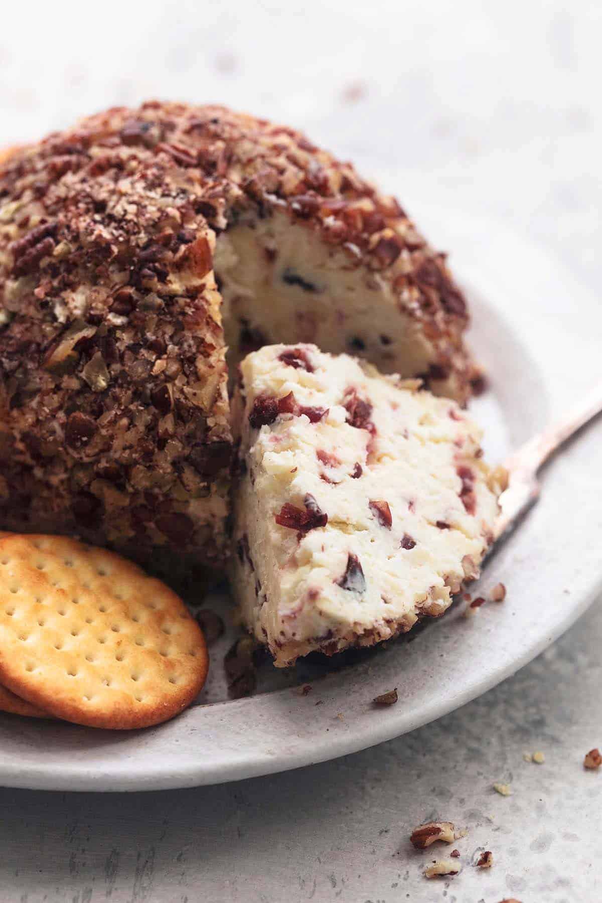 a cranberry pecan cheeseball wedge on a white plate with crackers.