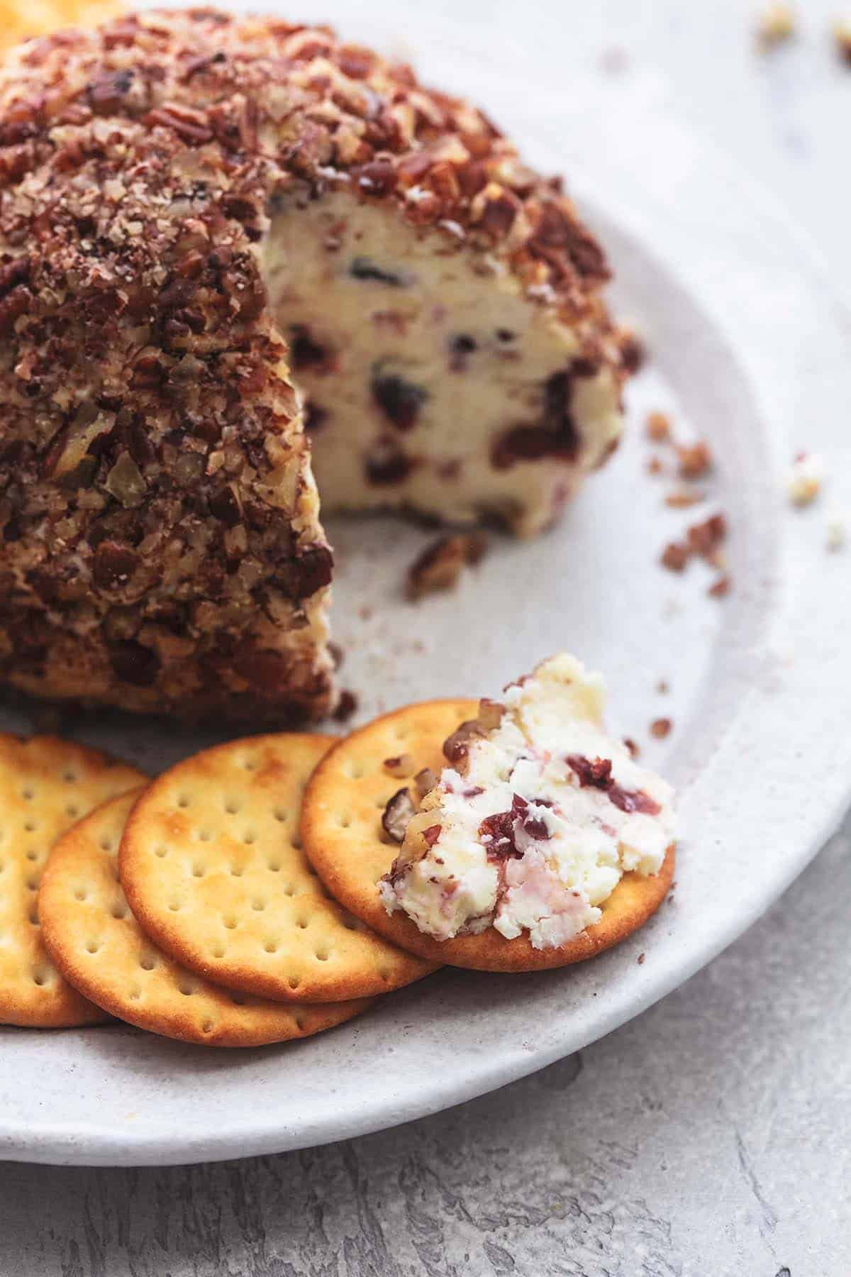 close up of a cranberry pecan cheeseball with crackers on a plate.