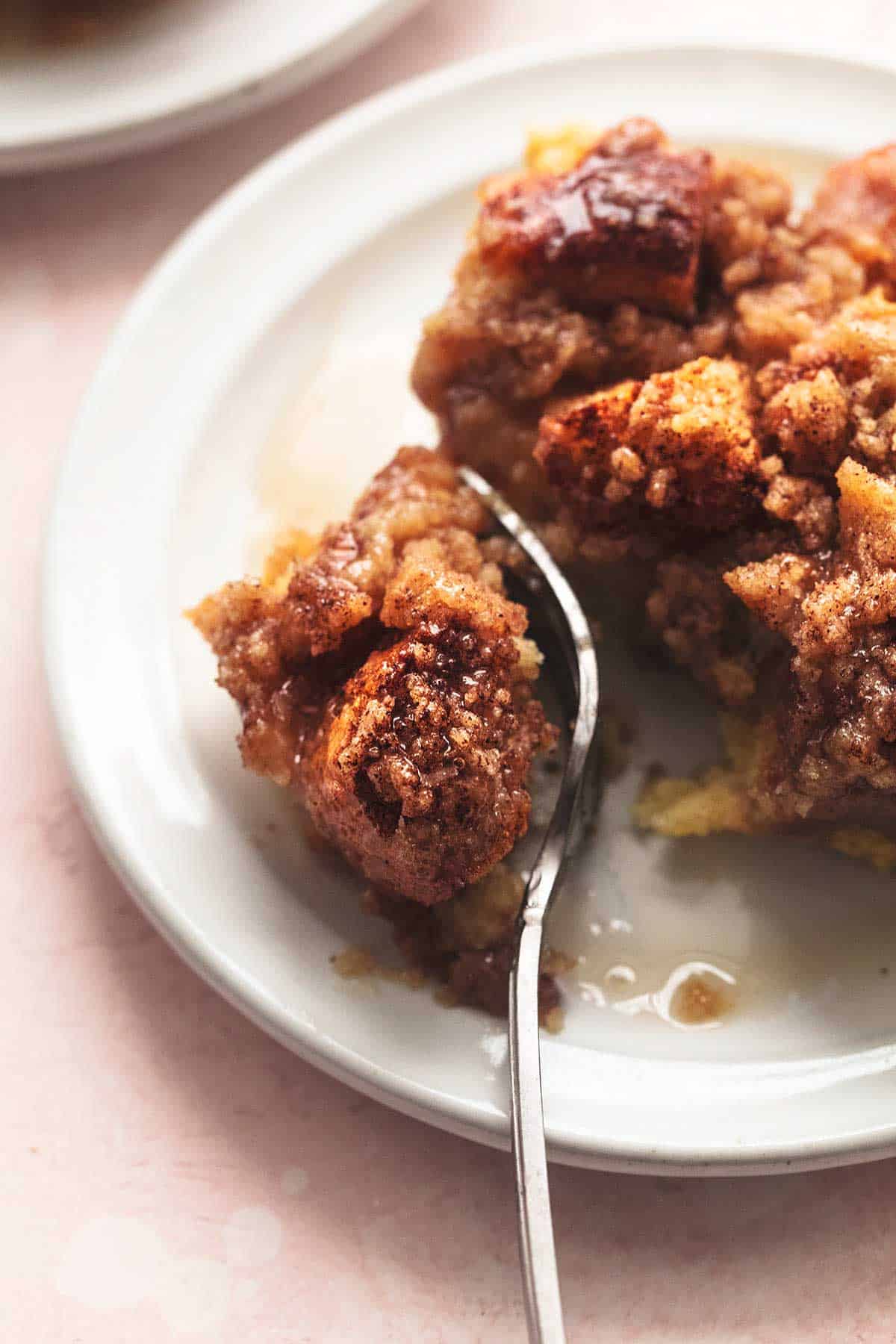 a piece of French toast casserole on a plate with a fork separating a bite from the rest of the piece.