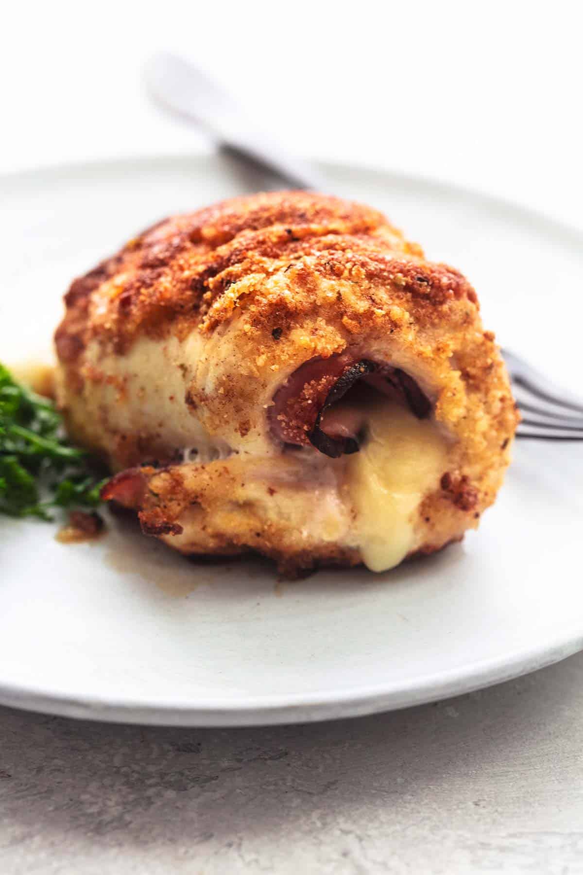 close up of a piece of chicken cordon bleu on a white plate with a fork.