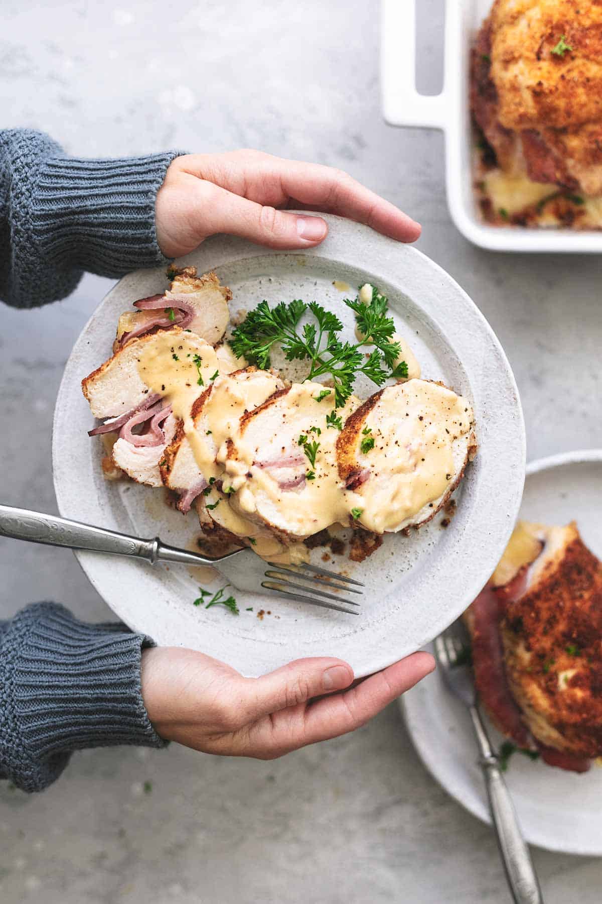 top view of hands holding a plate of chicken cordon bleu with Dijon cream sauce sliced.