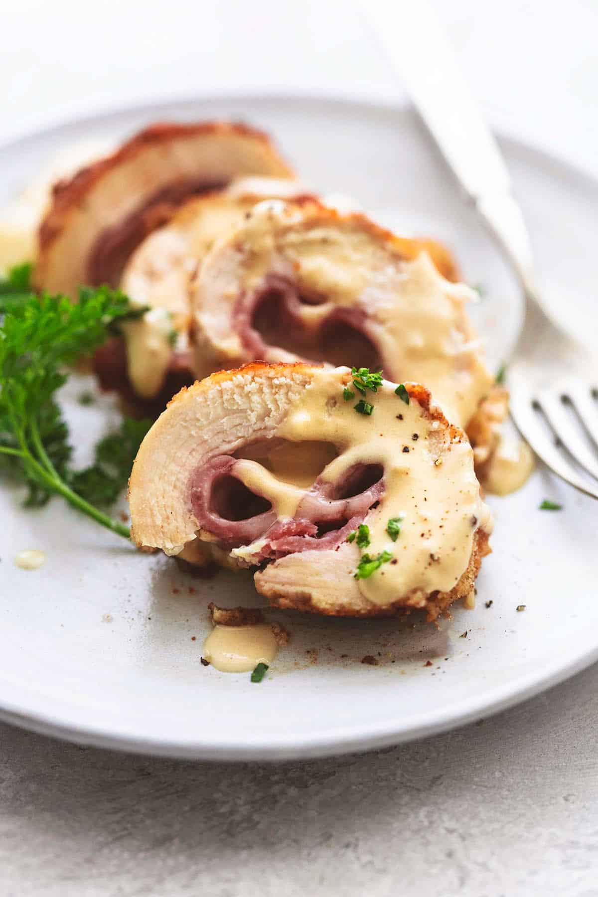 close up of sliced chicken cordon bleu with Dijon cream sauce with a fork on a plate.