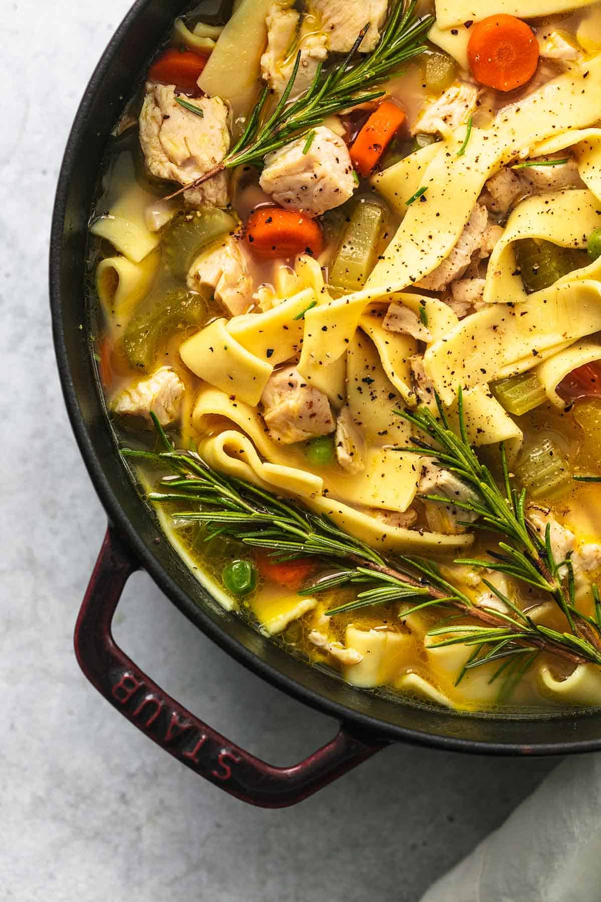 close up top view of chicken noodle soup with rosemary in a pot.