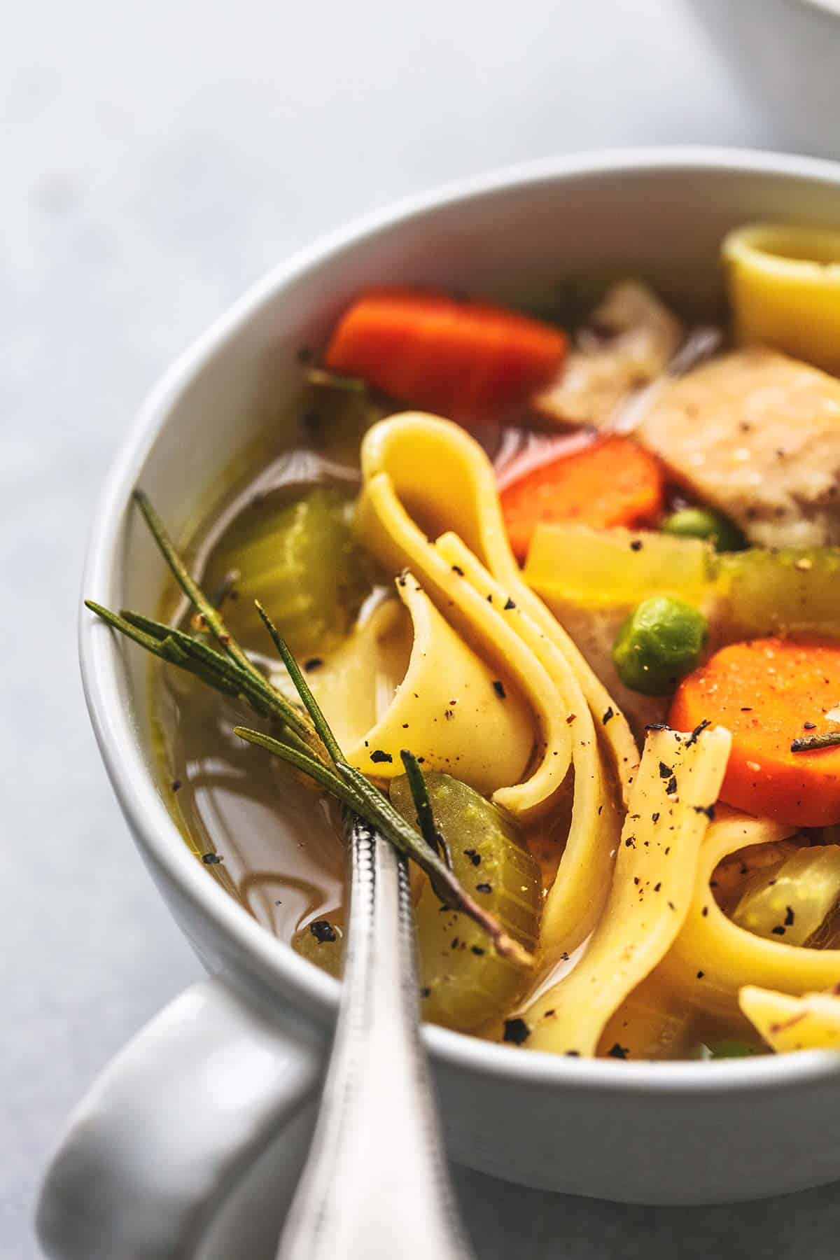 close up of chicken noodle soup with a spoon in a small bowl.