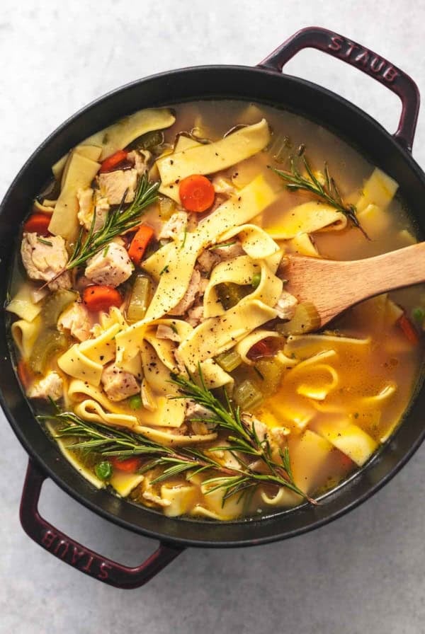 overhead view of serving spoon in pot of noodles with broth and chicken