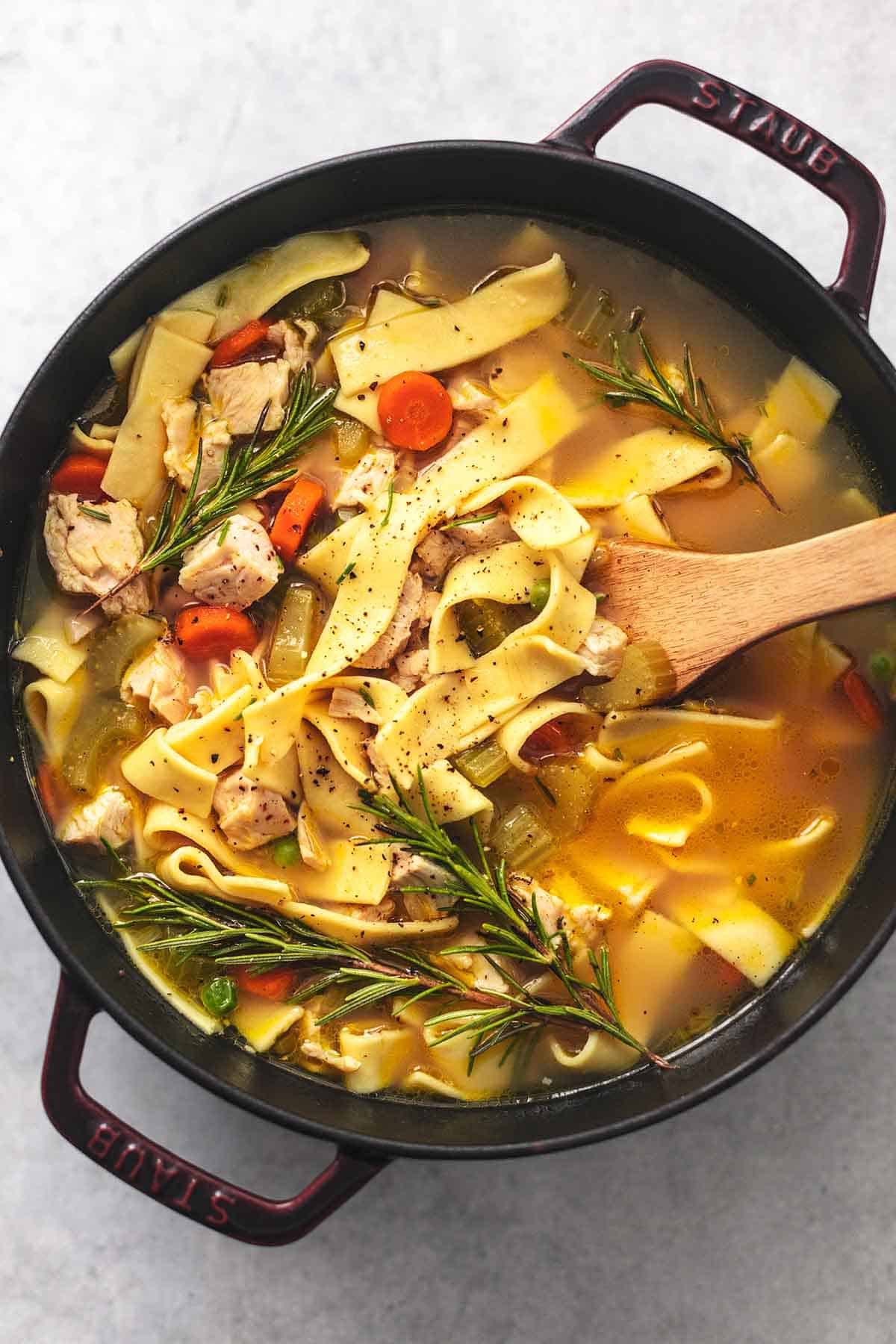 top view of chicken noodle soup with a wooden spatula in a pot.