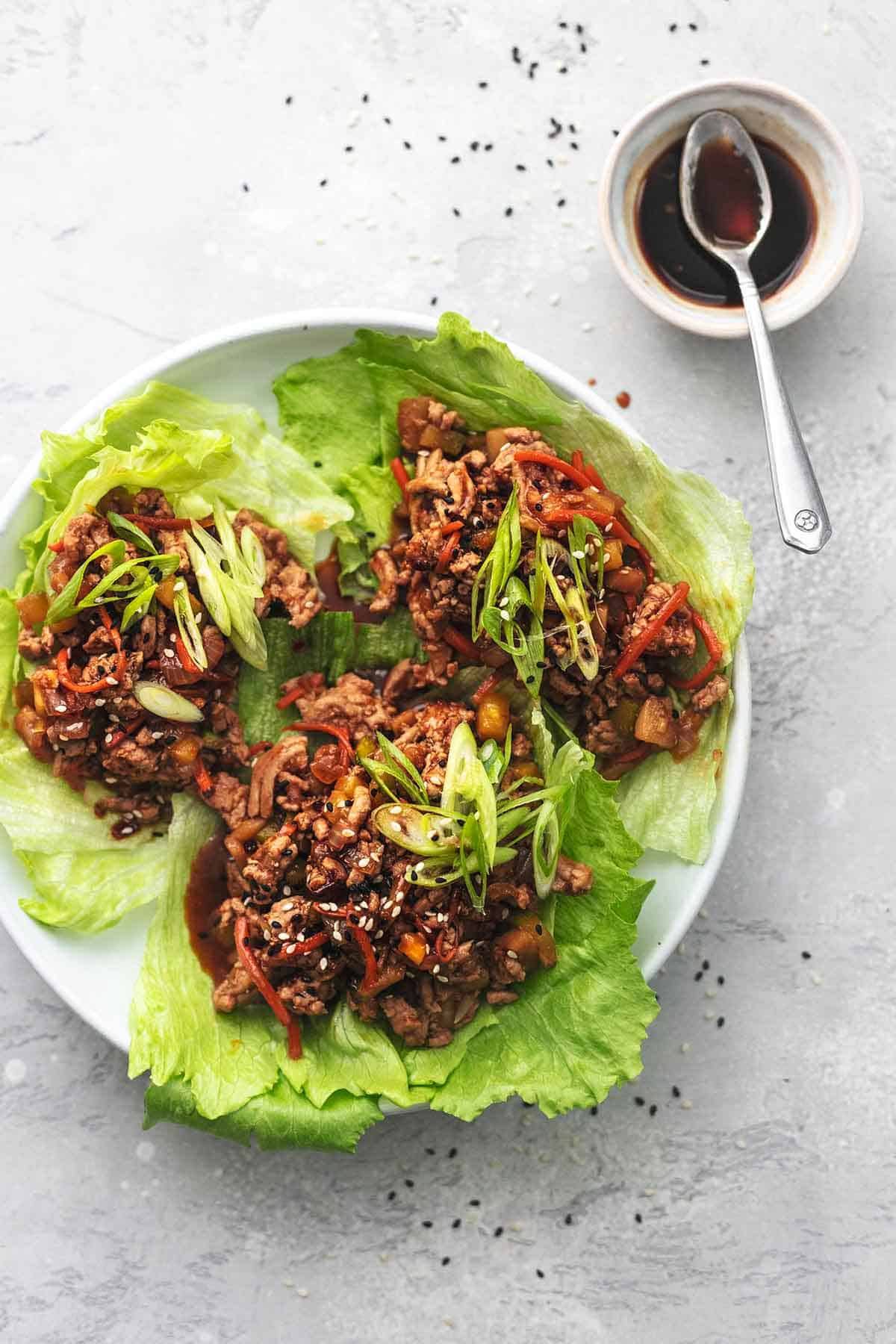 overhead view of three lettuce cups with pork and veggie filling with dark sauce in small bowl