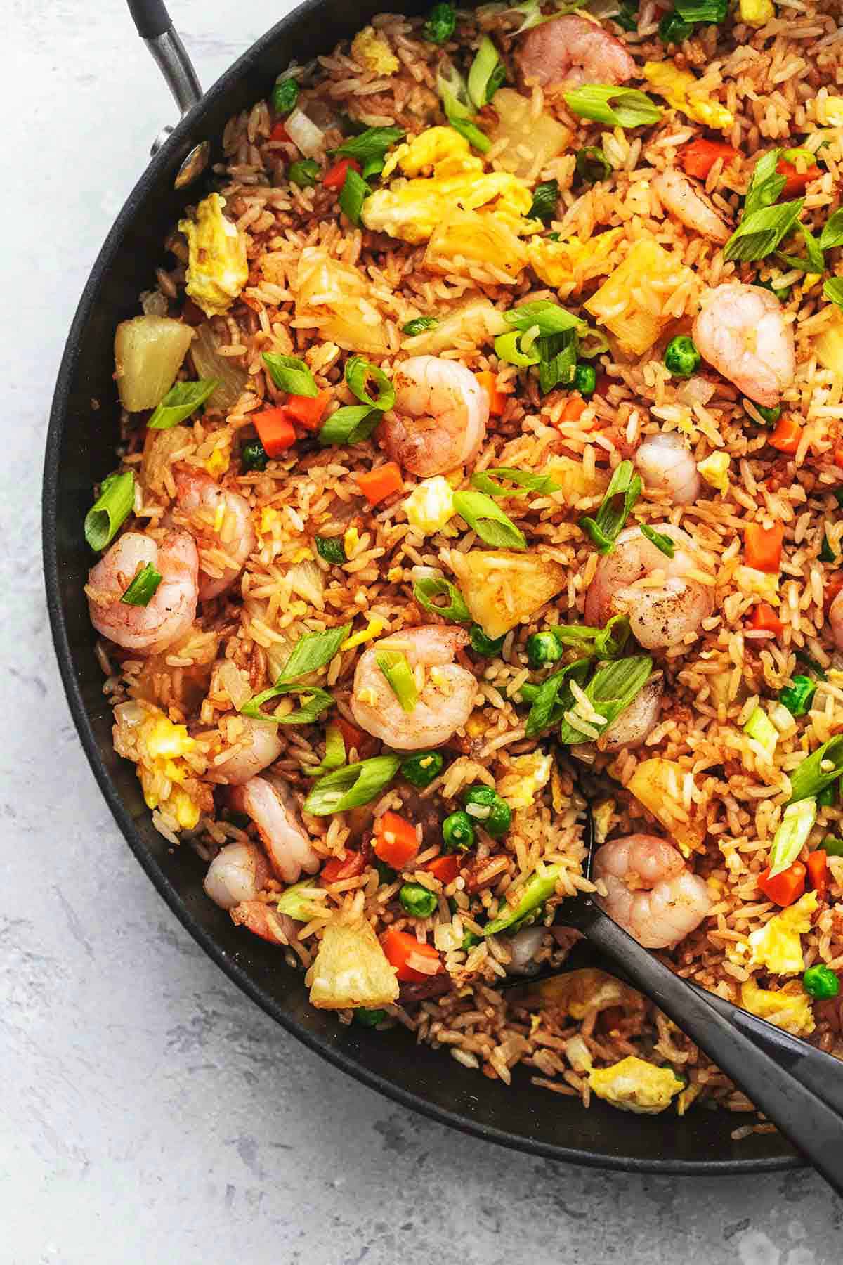 close up top view of shrimp fried rice with a serving spoon in a skillet.