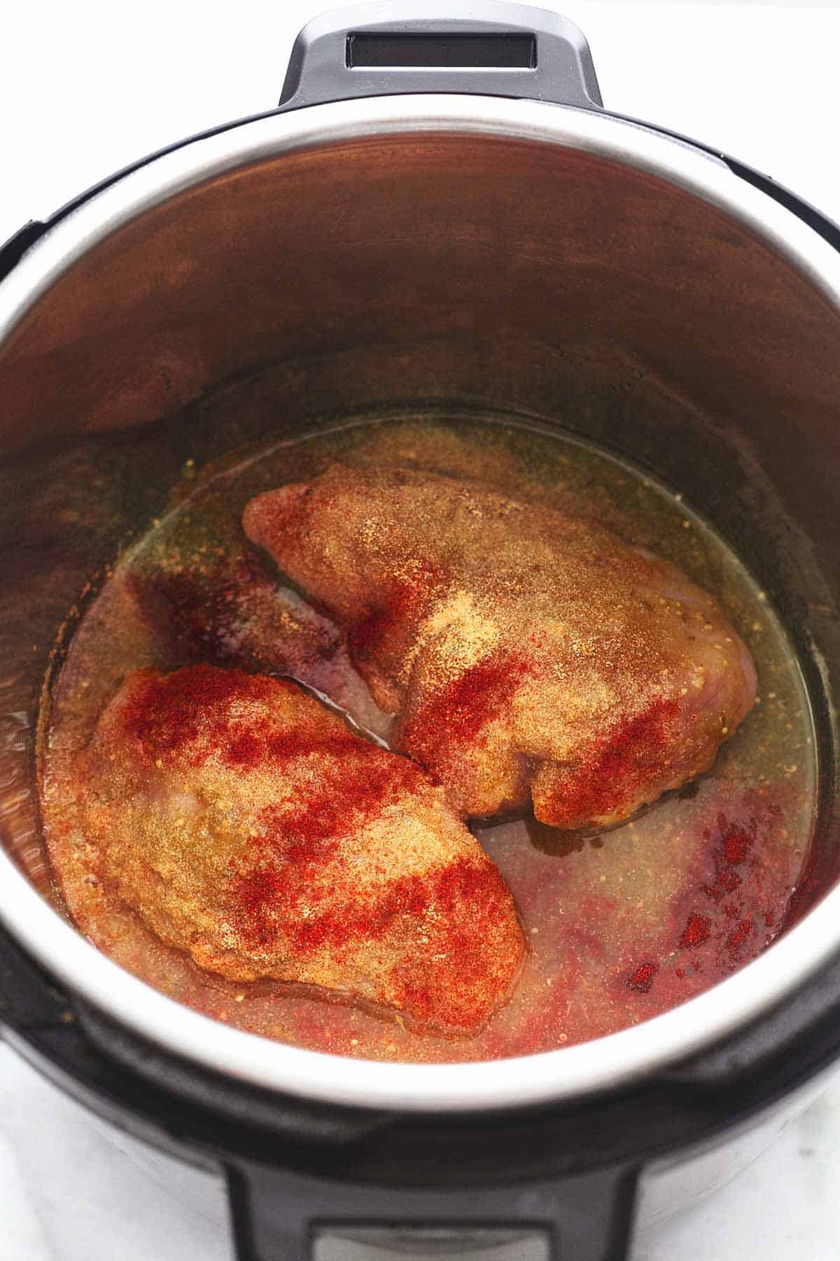 whole uncooked chicken breasts with liquid and spices in a slow cooker.