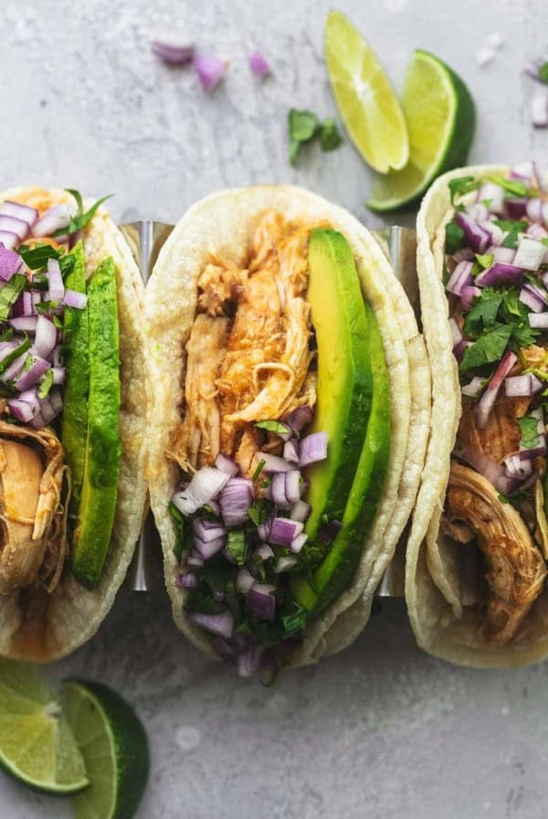 overhead view of three tacos in corn tortillas with shredded chicken and avocado slices