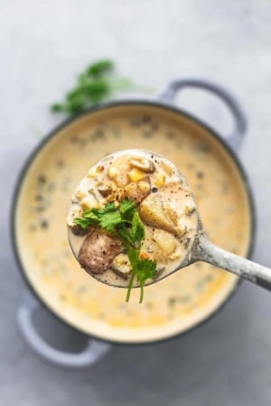 overhead view of ladle full of potatoes and yellow liquid with cilantro over pot of soup