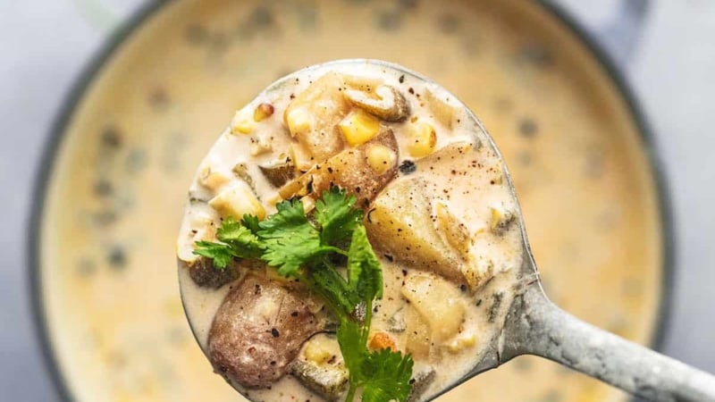 overhead view of ladle full of potatoes and yellow liquid with cilantro over pot of soup