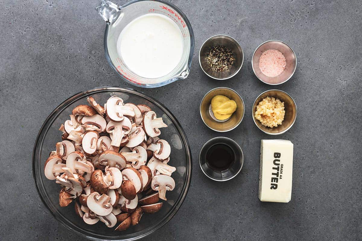 ingredients portioned into bowls including milk, sliced mushrooms, yellow sauce, pink salt, minced garlic, and a stick of butter