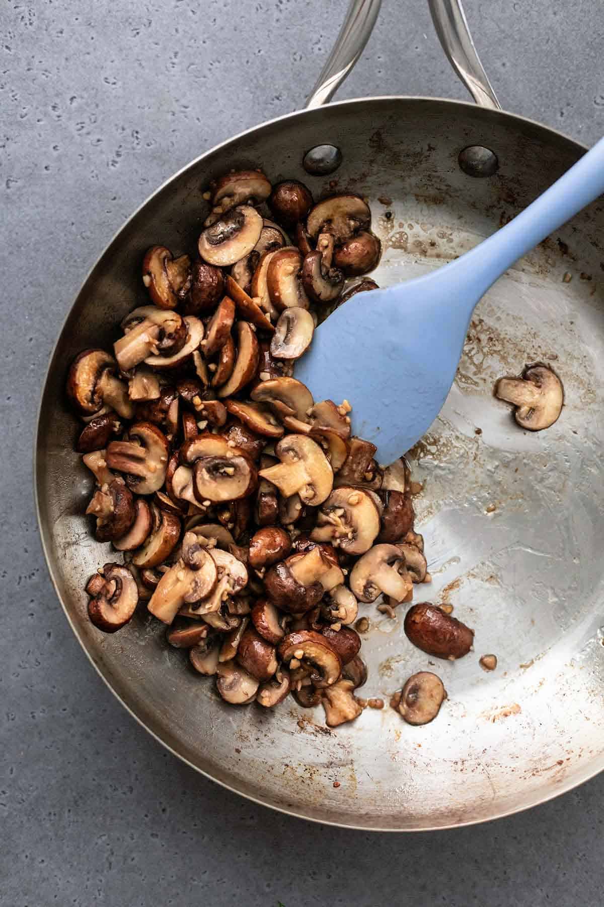 silicone spatula stirring browning sliced mushrooms in pan