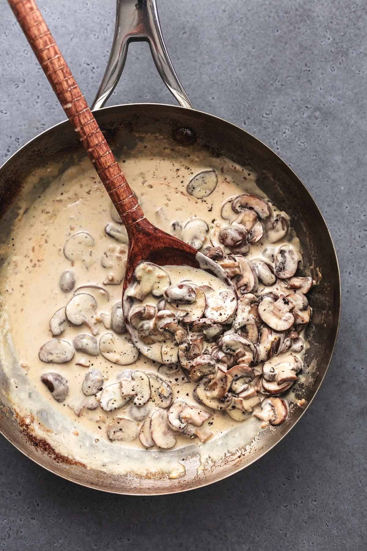 overhead view of stainless steel skillet with creamy sauce and sliced mushrooms with wooden spoon