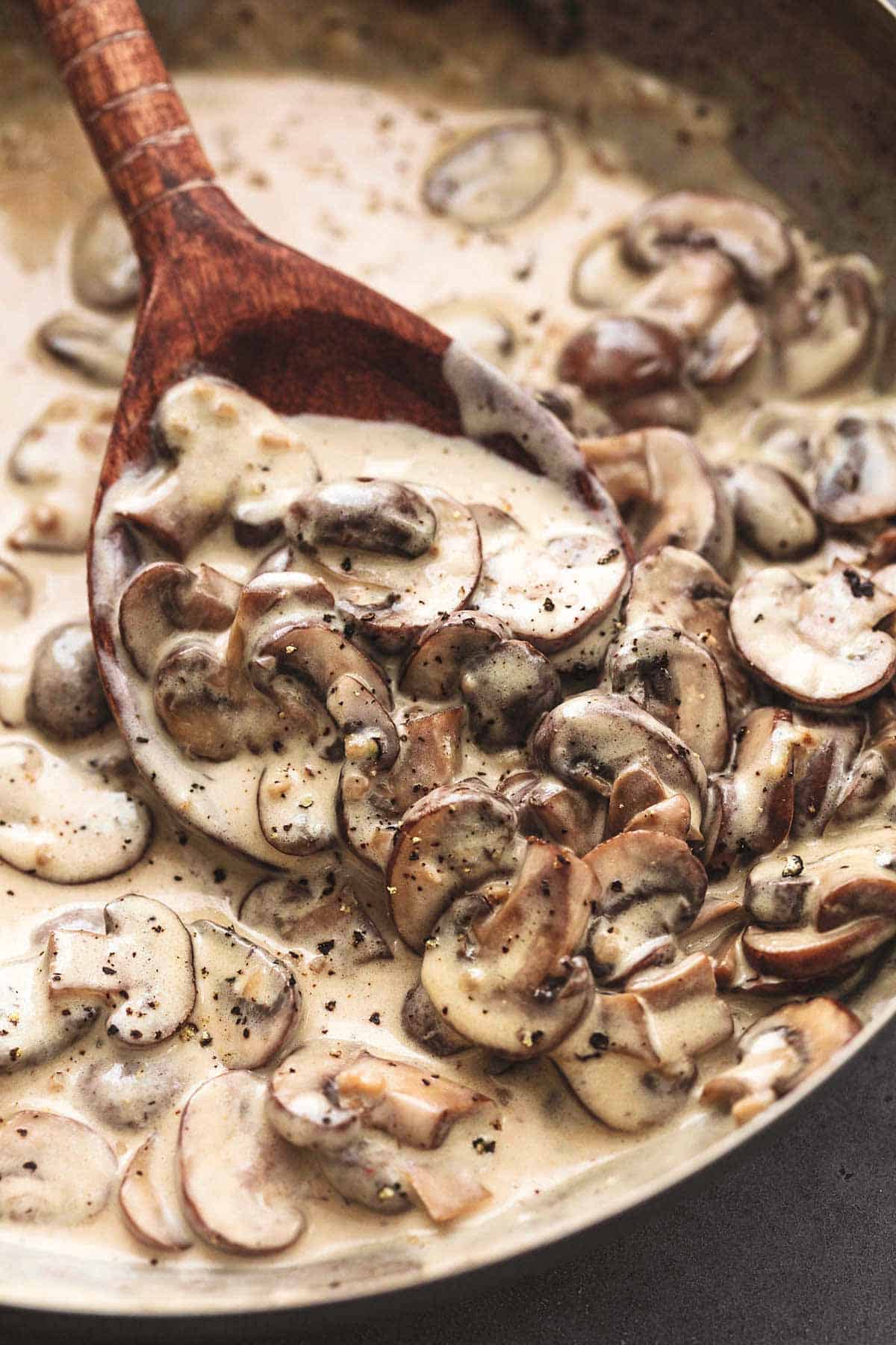 wooden spoon scooping mushrooms in creamy sauce with garlic