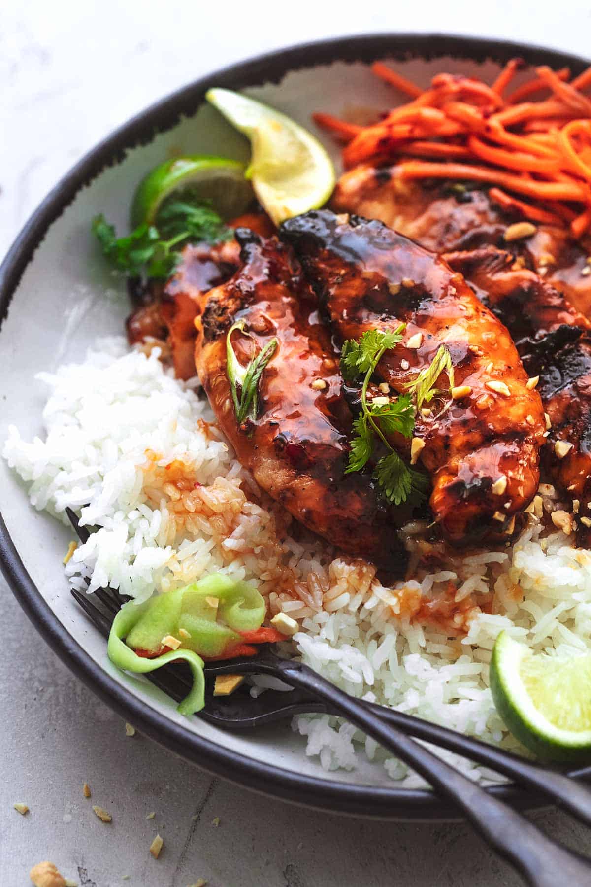 close up of sweet and spicy Thai chicken with ribbon vegetables, cilantro and rice on a plate.