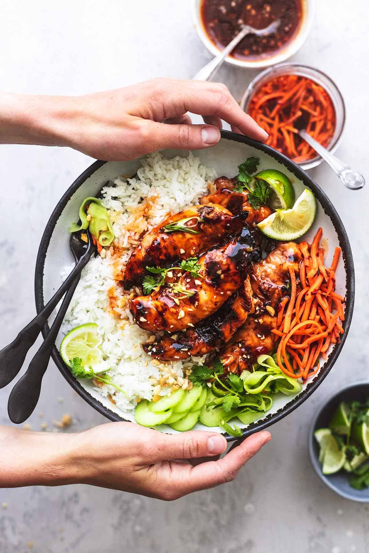 top view of hands holding a plate of sweet and spicy Thai chicken, rice, and veggies.