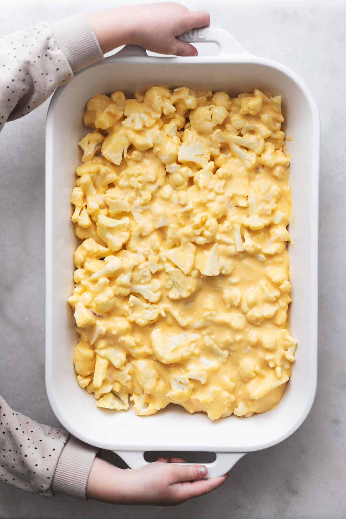 top view of a child's hands holding a baking pan with baked cauliflower mac and cheese in it.