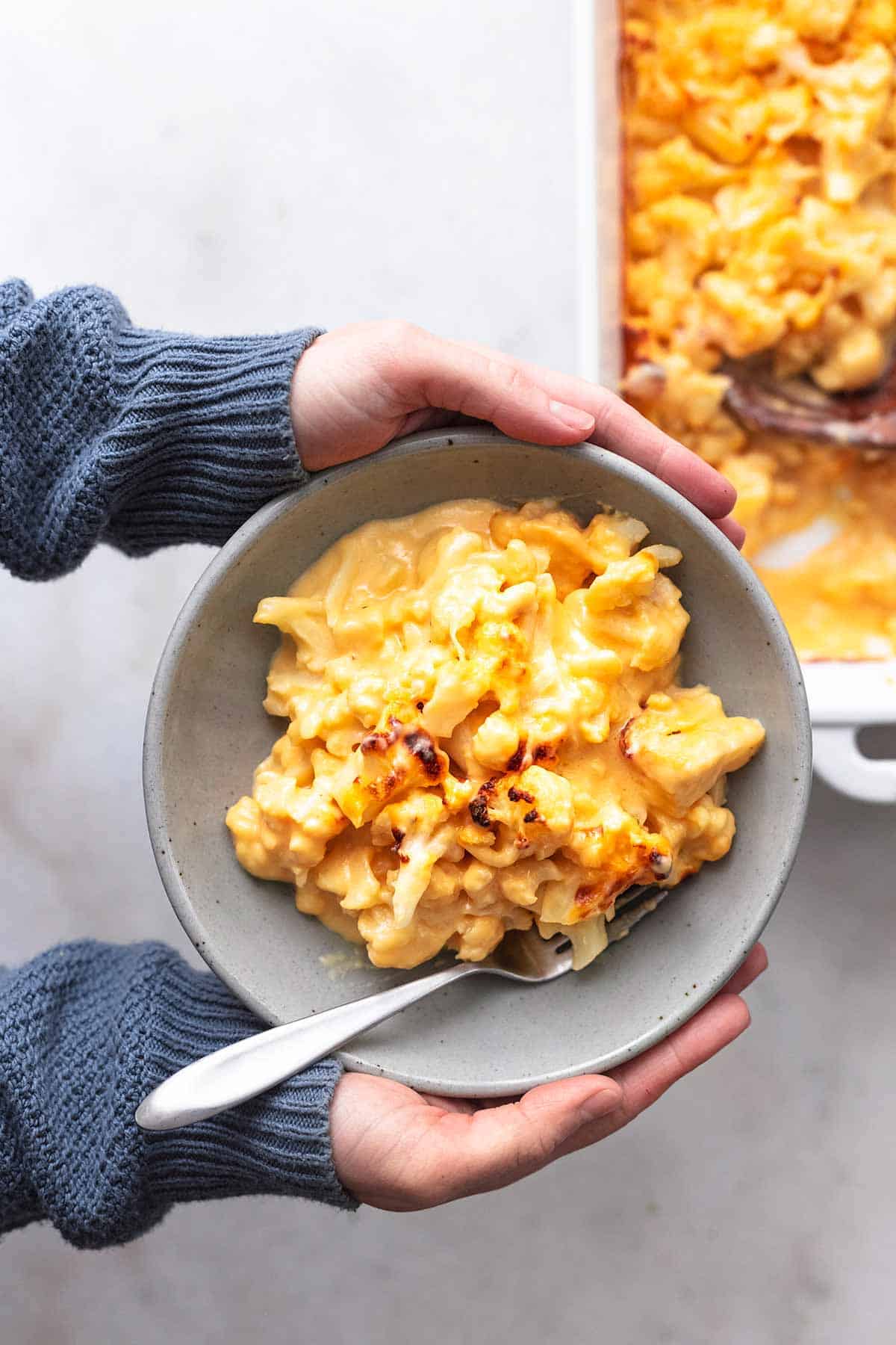 top view of hands holding a bowl of baked cauliflower mac and cheese with a fork.