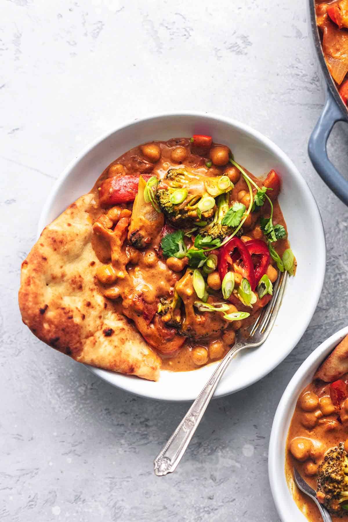 chickpea curry with naan bread and fork in white bowl on gray tabletop