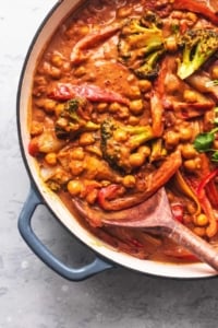 overhead view of half of a skillet with serving spoon and red curry with vegetables and chickpeas