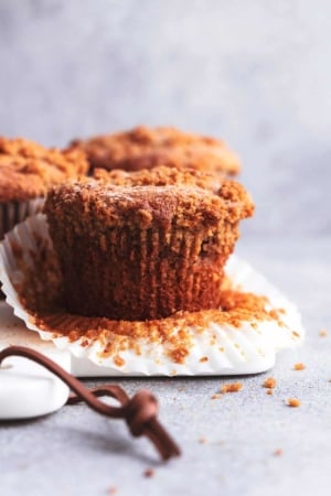 90 degree angle view of single cinnamon muffin with paper pulled back atop marble cutting board