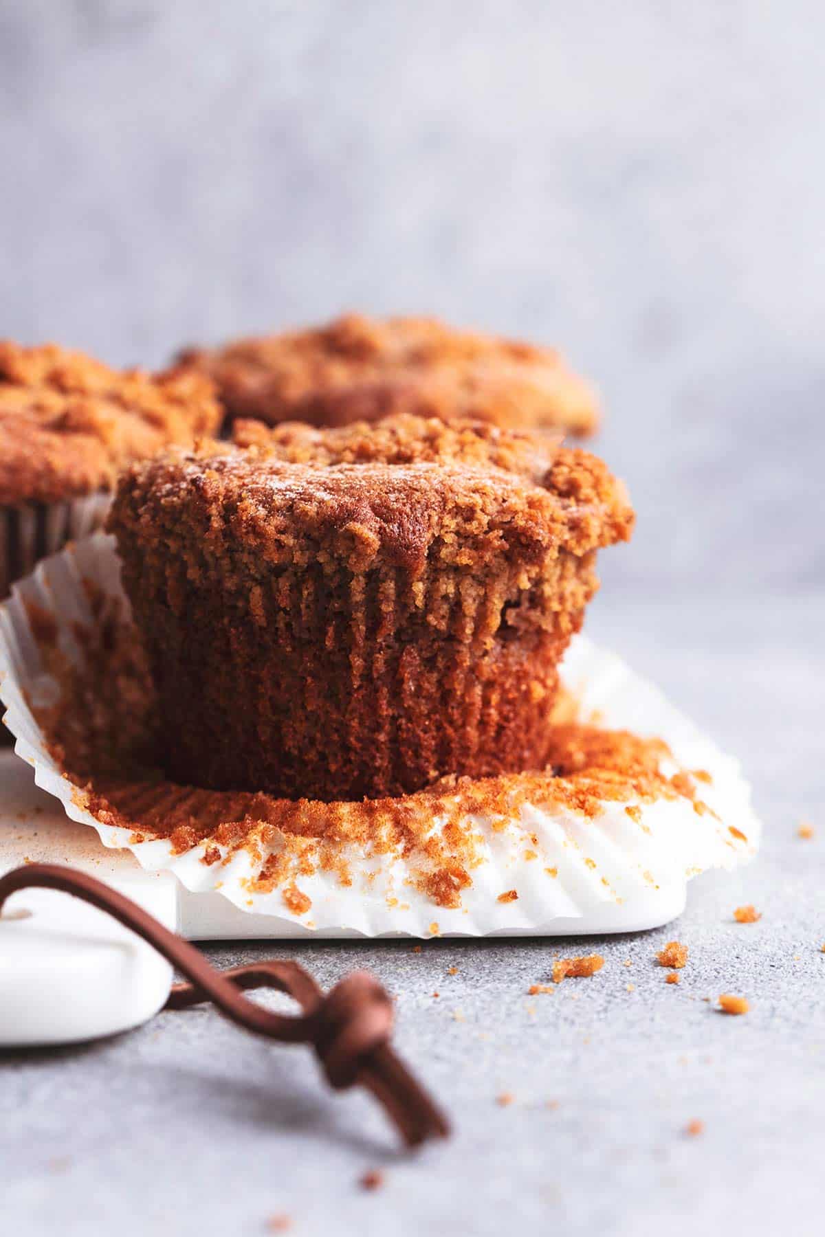 a cinnamon streusel muffin with the liner pulled back with more muffins behind it.