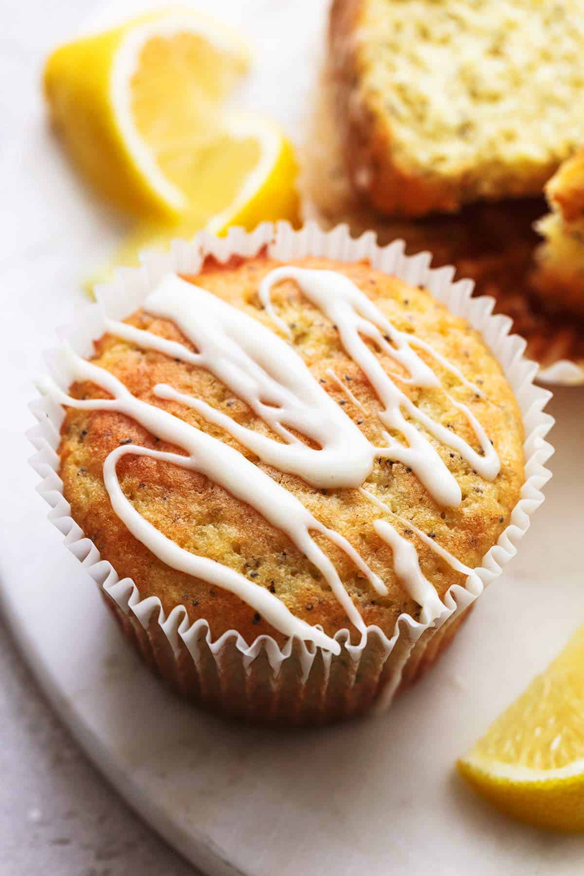 close up of a lemon poppyseed muffin with glaze and lemon wedges on the side.