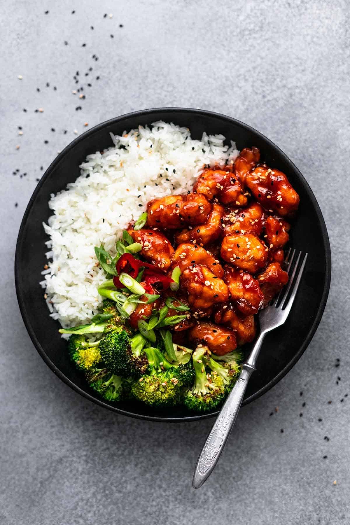 top view of sticky sesame chicken with rice and veggies on a plate with a fork.