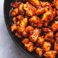 chicken pieces cooked in red brown sauce in black skillet