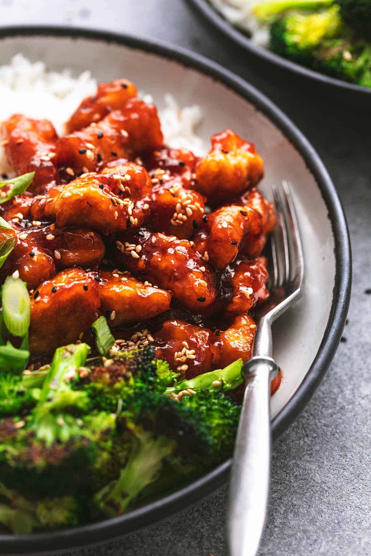 close up of sticky sesame chicken with broccoli and rice on the side on a plate.