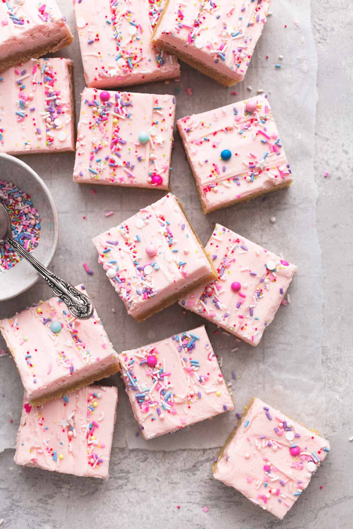 overhead view of a dozen sugar cookie bars on table with bowl of sprinkles and spoon