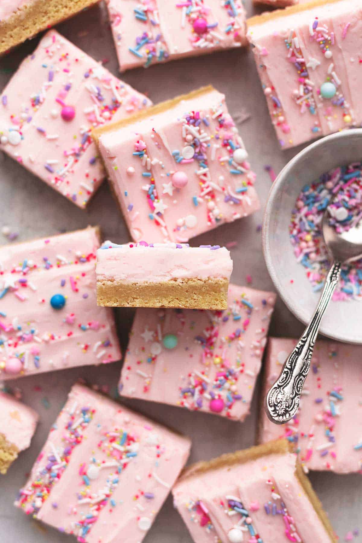 overhead view of dessert bars with sugar cookie base and buttercream frosting on top with bowl of sprinkles