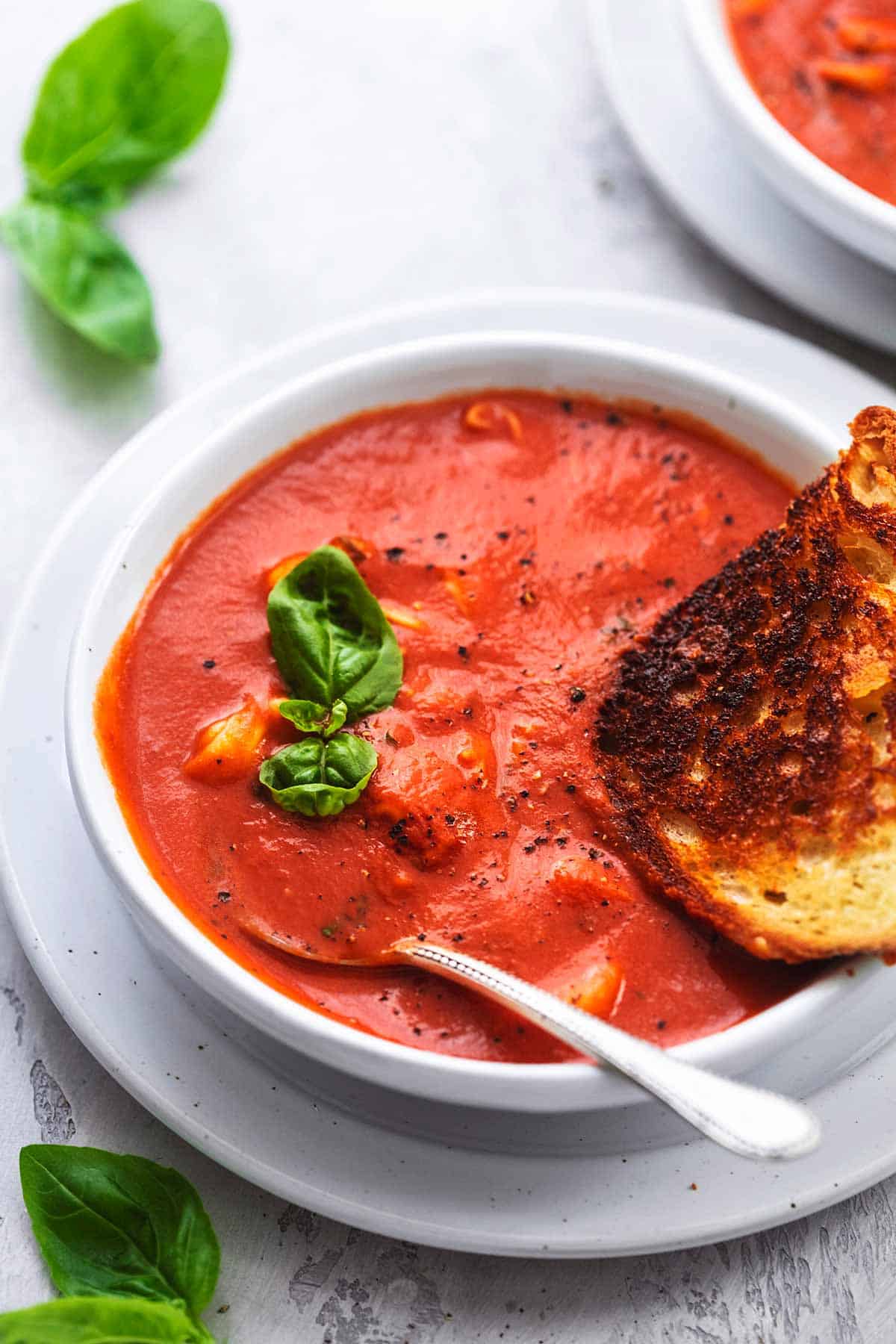 close up of tomato basil soup with grilled cheese and a spoon in a bowl.