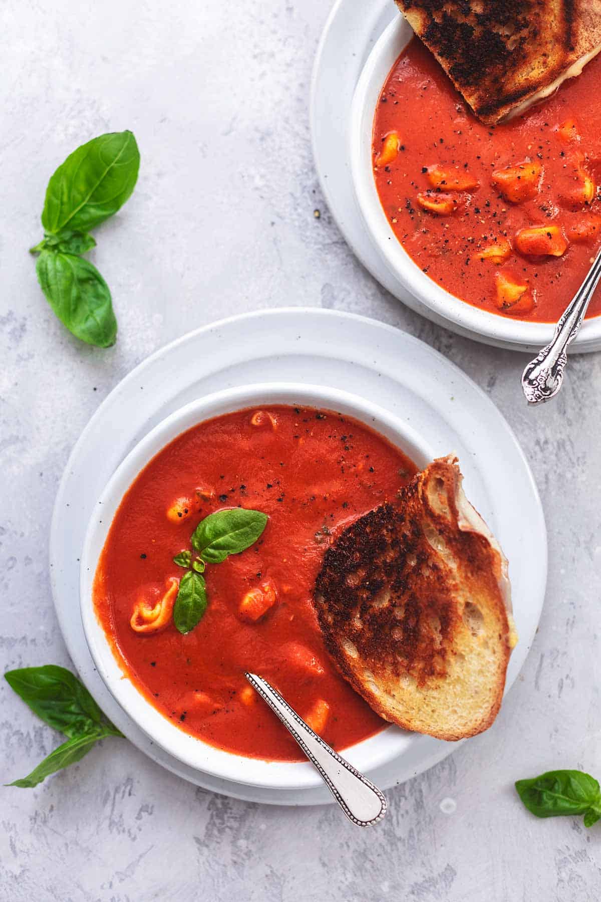 top view of two bowls of tomato basil soup with grilled cheese and basil.