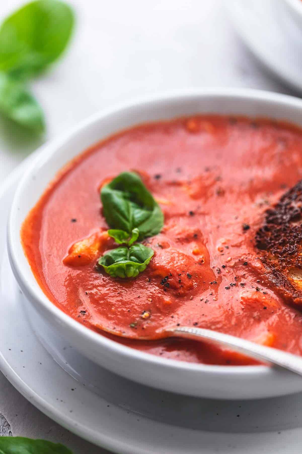 close up of tomato basil soup with a spoon in a bowl.