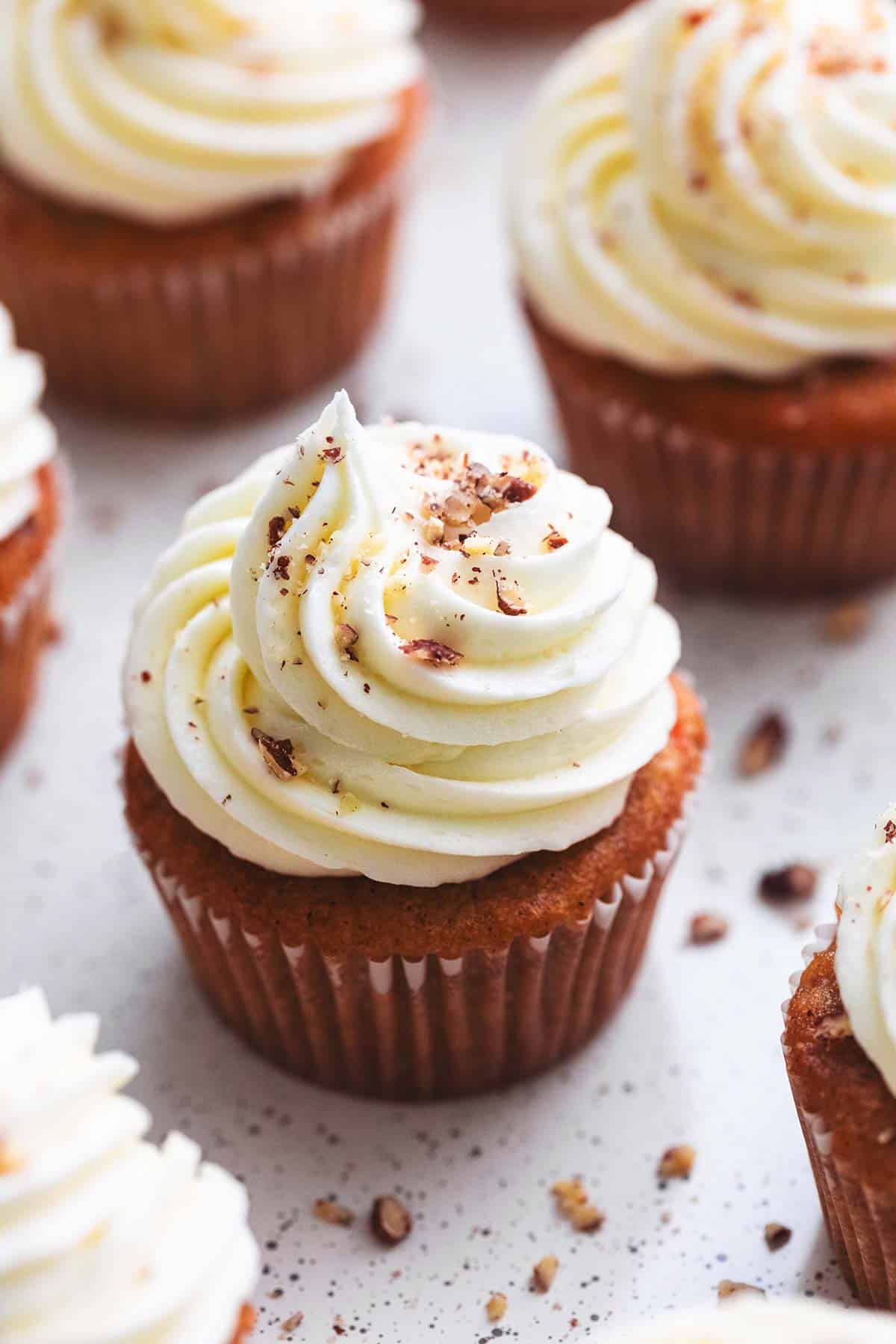 close up of a carrot cake cupcake with cream cheese frosting with more cupcakes around it.