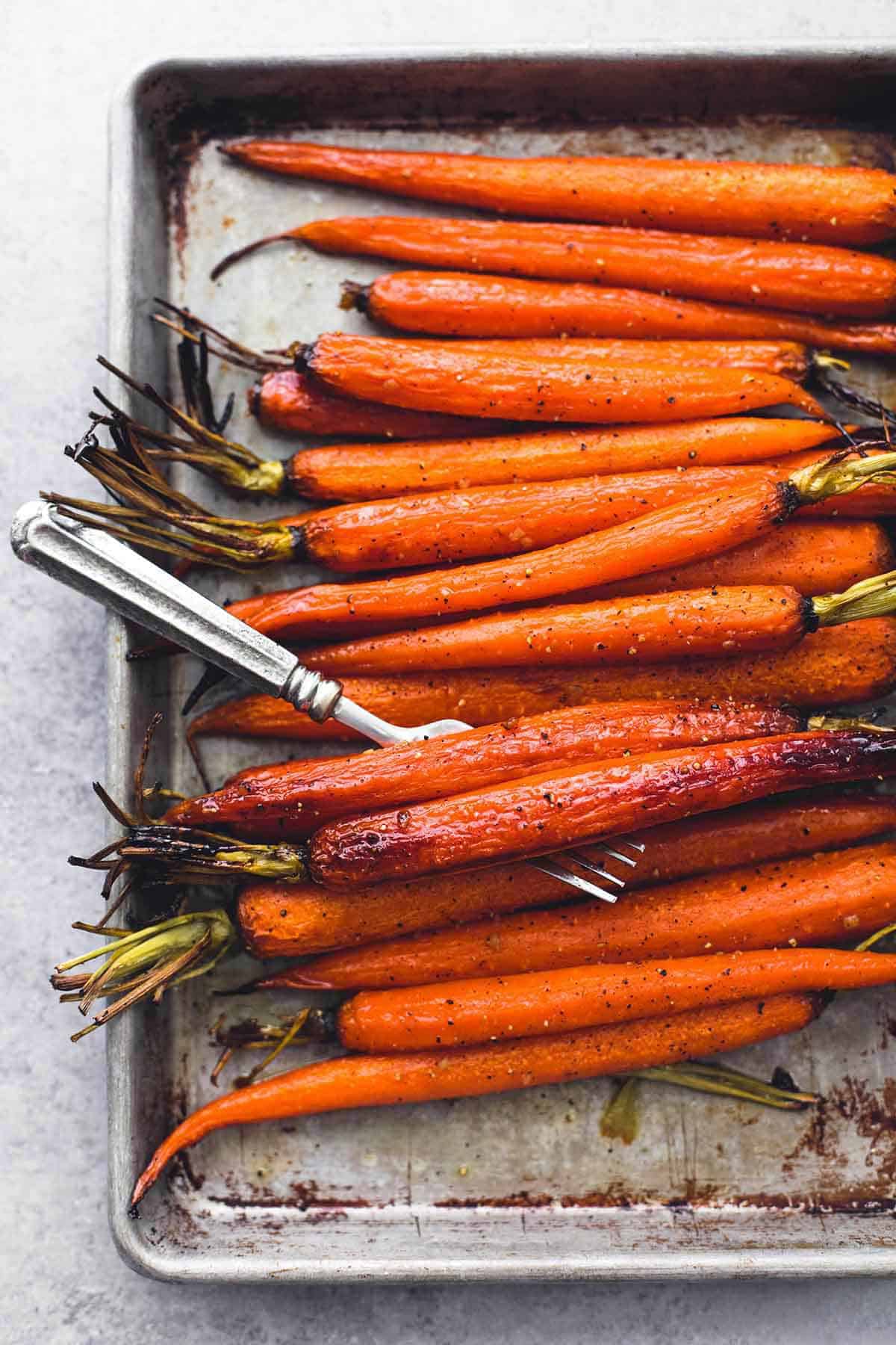 close up top view of honey brown sugar roasted carrots with a fork on a baking sheet.